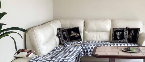 A beige leather sofa with patterned cushions, a small wooden coffee table, and two framed artworks on the wall.