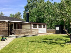 En enplansbyggnad med en uteplats, en möblerad, överbyggd sittplats och ett litet förråd.