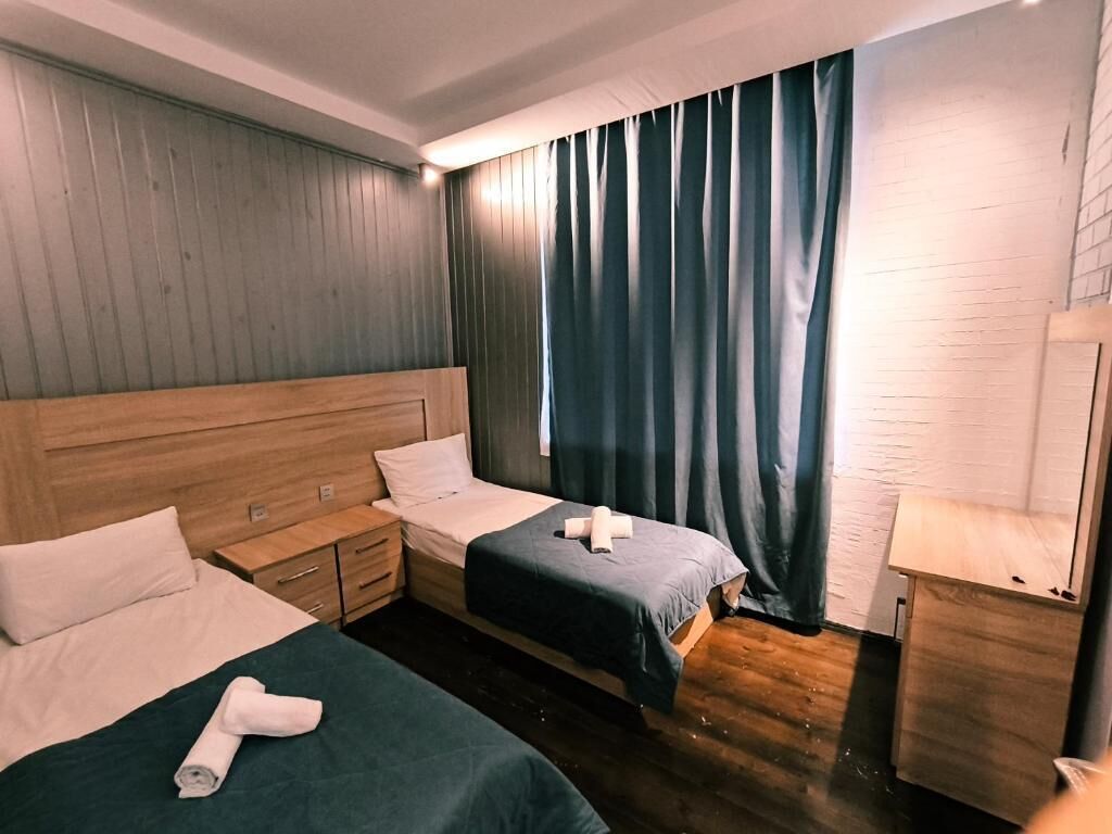 A hotel room with two beds, wooden headboards, a nightstand, a lamp, and a window with curtains.
