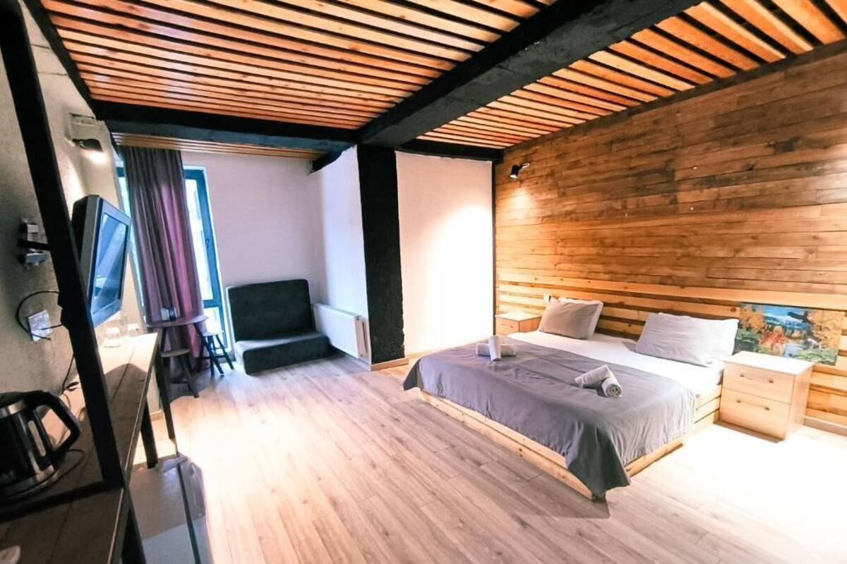 A bedroom with a wooden ceiling, a bed with pillows, a bedside table, and a TV.