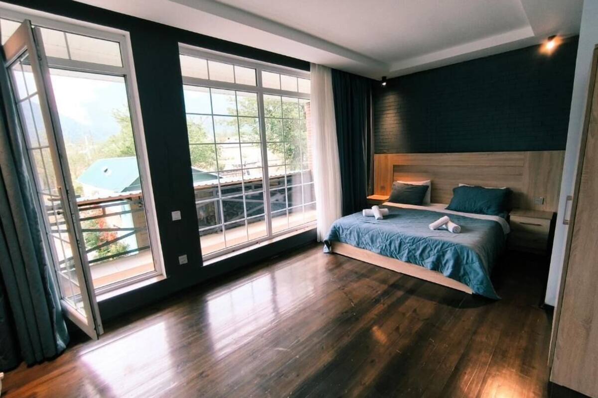 A bedroom with a large window, a bed, and a wooden floor.