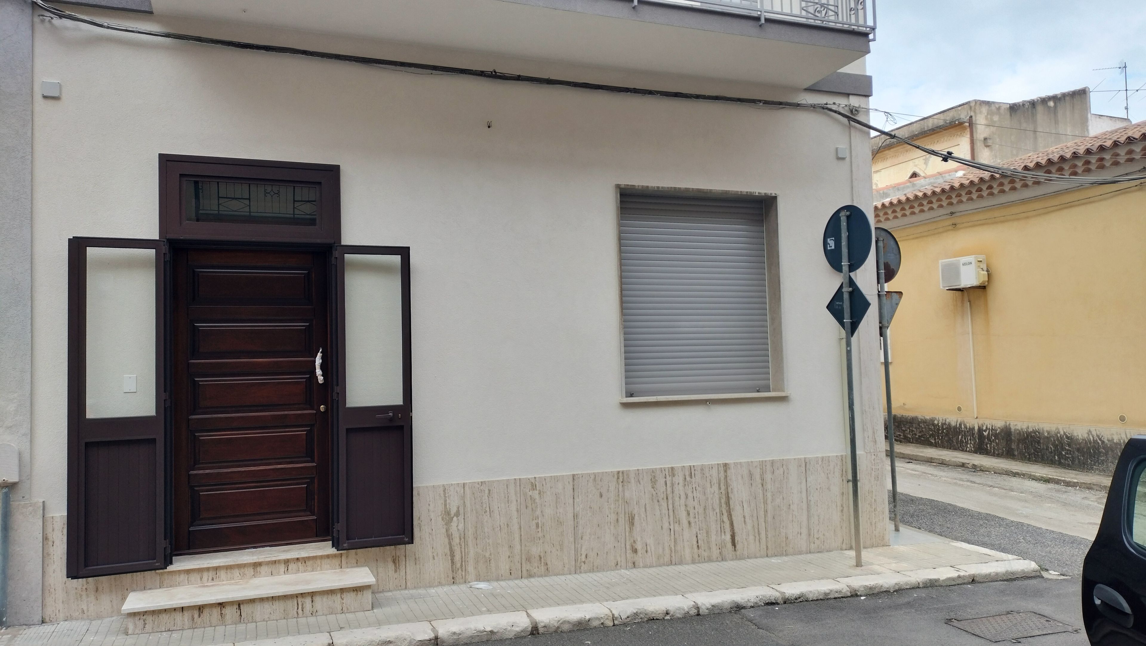 Un edificio con una porta in legno, una finestra con persiane e un cartello stradale.