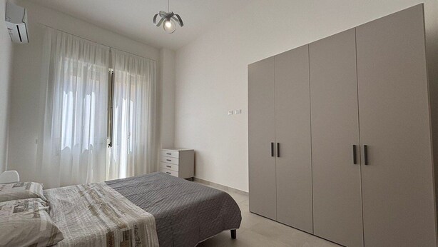 A bedroom with a bed, a wardrobe, a bedside table, and a window with curtains. - Civico 53 Apartments (Avola)