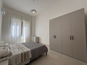 Ein Schlafzimmer mit Bett, Kleiderschrank, Nachttisch und einem Fenster mit Vorhängen.