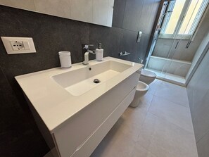 Ein modernes Badezimmer mit einem weißen Waschbecken, dunkel gefliesten Wänden, einer Toilette und einer Duschkabine.