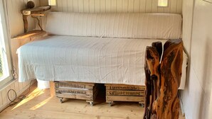 Interno di una baita in legno con un letto, uno scaffale e una scultura in legno originale.