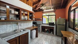 Een keuken met betegelde vloer, houten kastjes, een spoelbak, een fornuis, een magnetron en een koelkast.