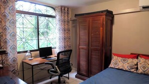 A bedroom with a bed, a desk with a computer, a wardrobe, and a window with patterned curtains. - Villa Las Maracas (Provincia de Guanacaste)