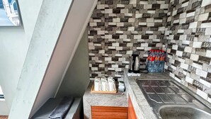 Cocina compacta con salpicadero de azulejos, un lavamanos de acero inoxidable, una encimera con hervidor y un cubo de basura.