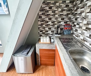 A compact kitchen with a tiled backsplash, a stainless steel sink, a countertop with a kettle, and a trash bin. - Cozzy Talaga Artea Pangalengan (bandung)