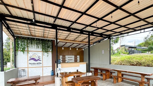 Un área de comedor al aire libre con bancos y mesas de madera, una barra de cocina y un logotipo en la pared.