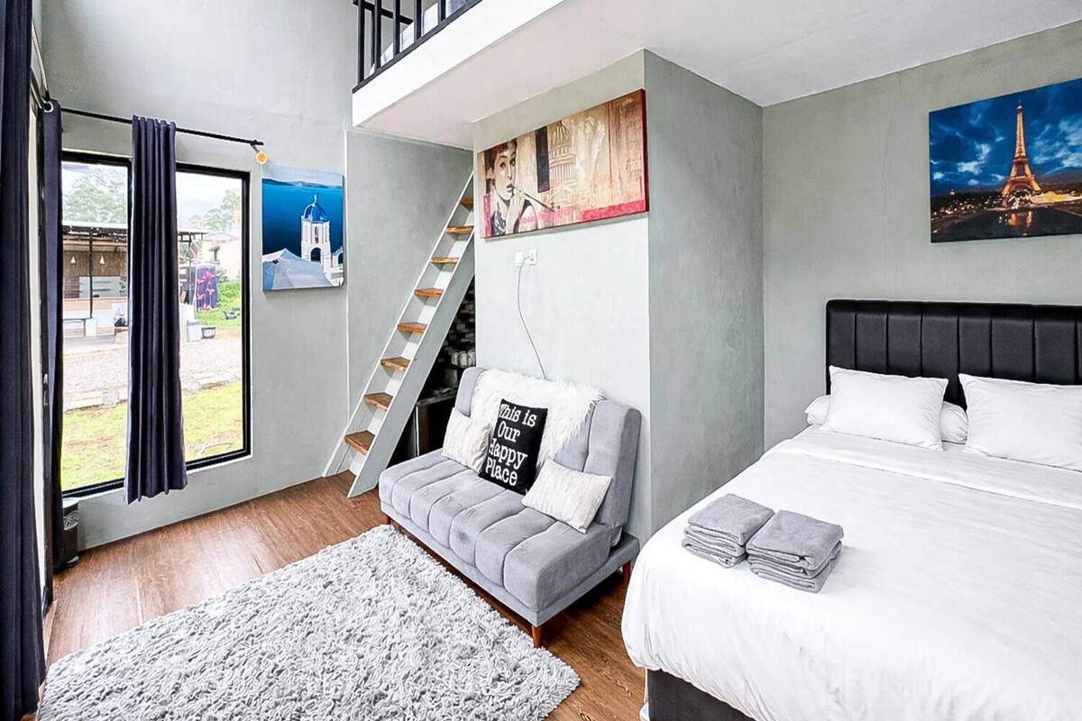 A bedroom with a bed, a sofa, a staircase, and a view of the Eiffel Tower.