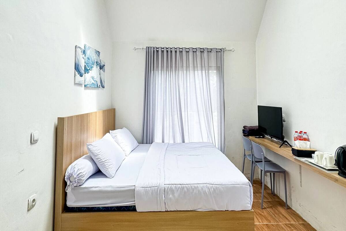 A bedroom with a bed, a desk with a computer, and a window with curtains.