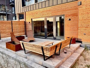 A modern outdoor seating area with wooden furniture and a glass door entrance.