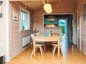 Un interior de madera con una mesa de comedor, sillas, una lámpara colgante y vistas al exterior.