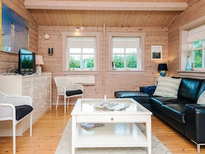 Un acogedor interior de cabaña con un aparador blanco, un sofá de cuero negro, una mesa de centro blanca y una silla blanca.