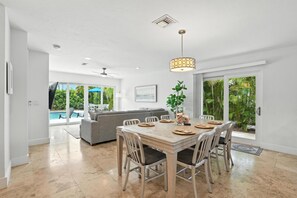 Ein geräumiger Essbereich mit Holztisch und -stühlen, Deckenventilator und Blick auf einen Pool und Grünflächen.