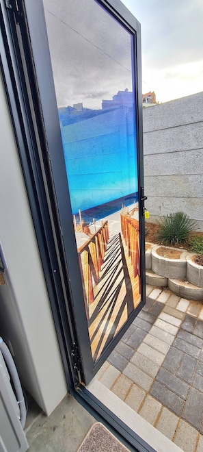 Uma porta de correr de vidro dá para uma varanda com vista para o mar e uma parede de pedra.