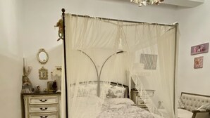 Un dormitorio con cama con dosel, cómoda, silla y candelabro.