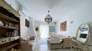 Una sala de estar con un sofá, una silla, una estantería, una araña y un cuadro en la pared.