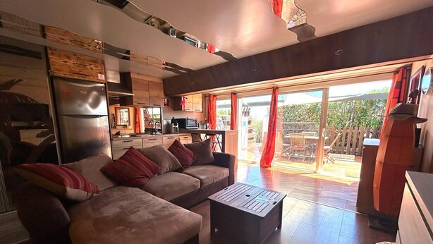 Een moderne woonkamer met een hoekbank, een salontafel en een keukenhoek met een koelkast en magnetron.