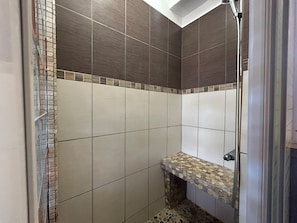 Eine Dusche mit gefliesten Wänden und Ablagefläche aus Stein.