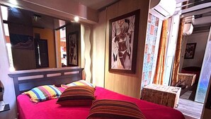 Een kamer met een bed, een spiegel, een raam met gordijnen en een schilderij aan de muur.