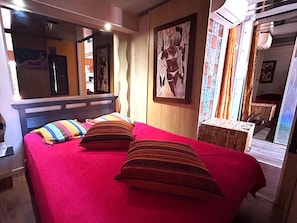 Ein Zimmer mit einem Bett, einem Spiegel, einem Fenster mit Vorhängen und einem Gemälde an der Wand.