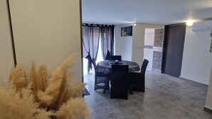 Un salon moderne avec un coin repas, une grande fenêtre ornée de rideaux légers et une plante en pot.