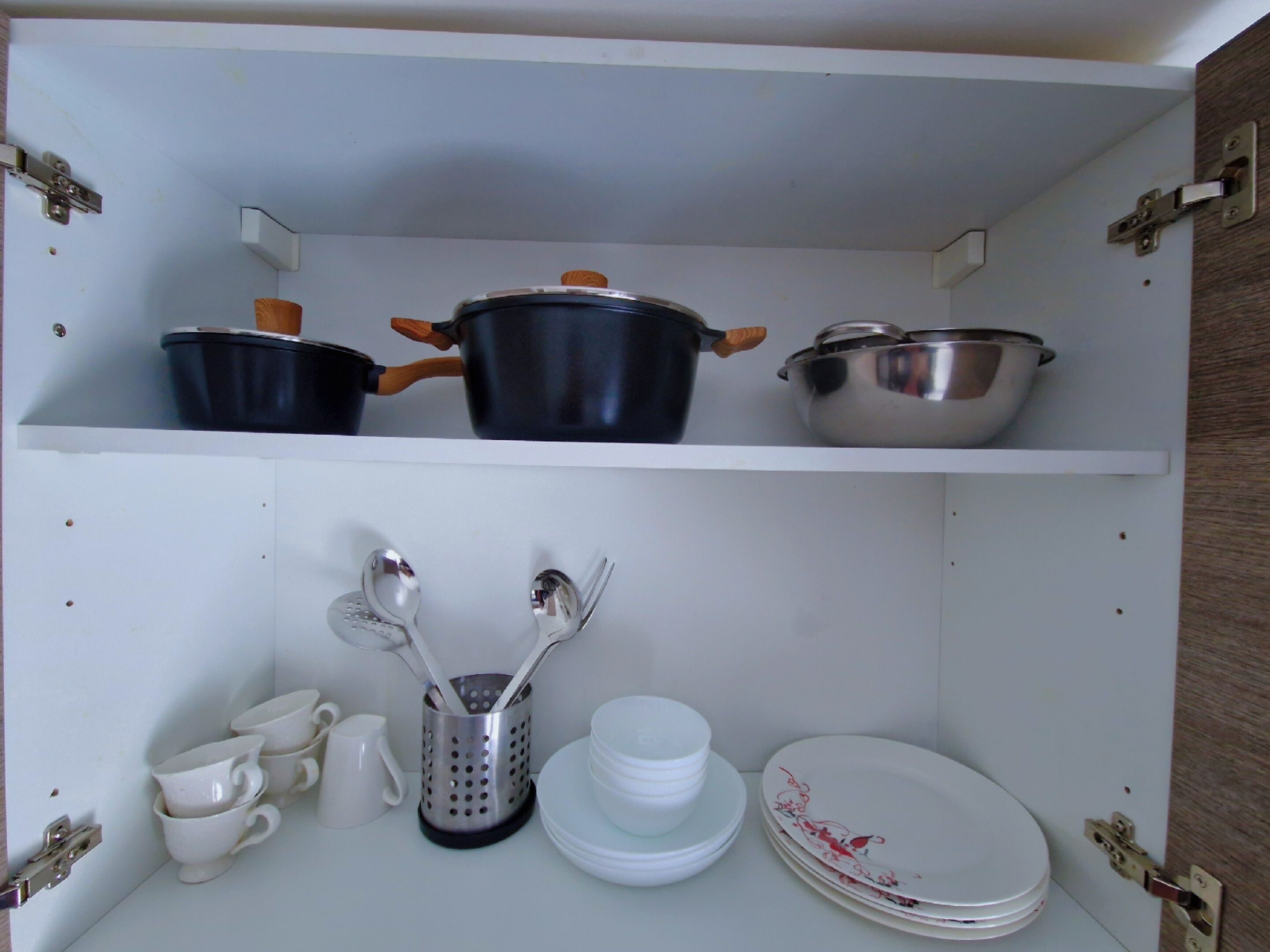 A kitchen cabinet with pots, utensils, and stacked dishes.