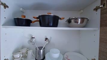A kitchen cabinet with pots, utensils, and stacked dishes.