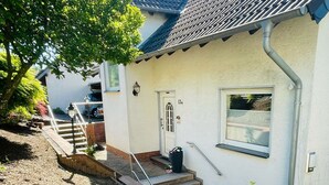 Ett hus med en vit fasad, en ytterdörr, en liten veranda med några trappsteg och ett fönster.