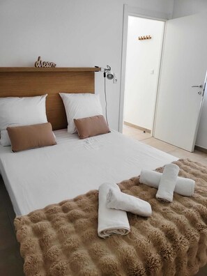 A neatly made bed with white and brown bedding, a fluffy brown throw blanket, and a bedside lamp.