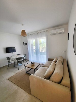 A living room with a sofa, a TV, a dining table, and a window with curtains.