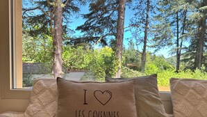 A bed with striped bedding and pillows, one with 'I ♥ LES CEVENNES' text, and a window view of a forest. - Just a 2-minute walk from downtown Anduze! Enjoy this new home surrounded by nature. (Anduze)