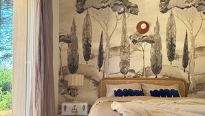 A bedroom with a bed, a window with curtains, a wall with a tree mural, and a bedside table. - Just a 2-minute walk from downtown Anduze! Enjoy this new home surrounded by nature. (Anduze)