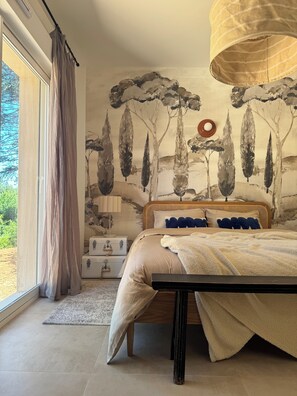 Ein Schlafzimmer mit Bett, Fenster mit Vorhängen, einer Wand mit Baum-Wandgemälde und einem Nachttisch.
