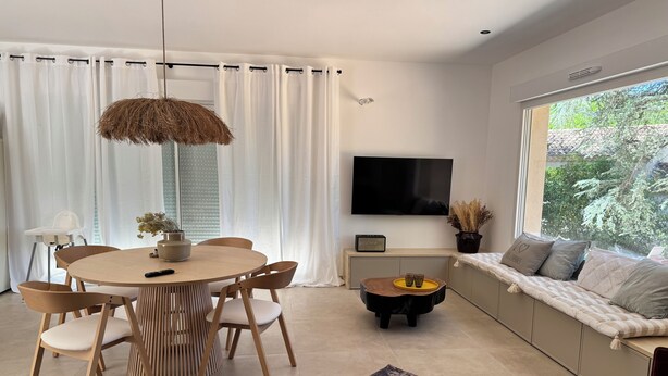A modern living room with a round wooden dining table, a sofa with a view to the outdoors, a flat-screen TV, and a potted plant. - Just a 2-minute walk from downtown Anduze! Enjoy this new home surrounded by nature. (Anduze)