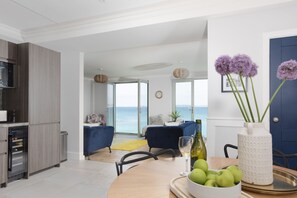 Eine moderne Küche mit integriertem Mikrowellenherd, einem Essbereich mit Holztisch und Blick auf das Meer durch große Fenster.