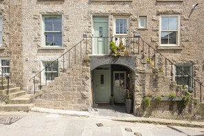 A stone building with a green door, a staircase with a metal railing, and a small balcony with plants. - Mermaids 2 - Sea views, direct beach access (St Ives)