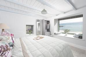 A bedroom with a bed, a window with a view of the sea, a hanging light fixture, and a wardrobe. - Mermaids 2 - Sea views, direct beach access (St Ives)