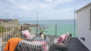 Ein Balkon mit Sitzgelegenheit im Freien, Blick auf das Meer und eine Steinmauer.