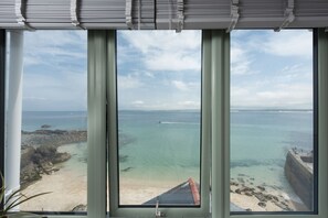 A view through a window with a view of the sea, a boat, and a sandy beach. - Mermaids 3 - Sea-facing property, direct beach access (St Ives)
