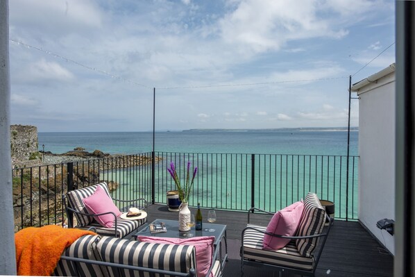 A balcony with a view of the sea, featuring a table with a bottle and glasses, striped chairs, and a stone wall. - Mermaids - Sea-facing properties, direct beach access (St Ives)