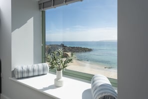 A room with a large window overlooking a rocky beach and calm sea. - Mermaids - Sea-facing properties, direct beach access (St Ives)