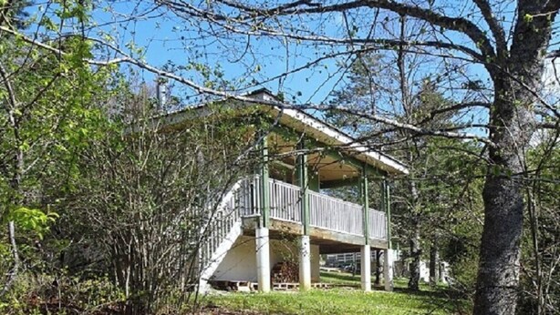 Una estructura al aire libre techada con una escalera que lleva a un balcón, rodeada de árboles y césped.