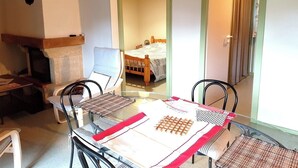 Una habitación con cama, una mesa con mantel individual, una silla, una mesita de noche con lámpara y una chimenea.