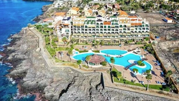 Et kysthotel med flere bygninger, et centralt poolområde og en klippefyldt kystlinje.
