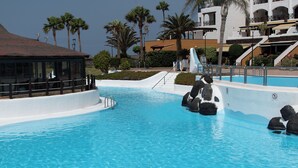 En swimmingpool med klippeformationer, et overdækket opholdsområde og en bygning med balkoner.