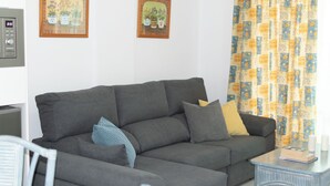 En grå hjørnesofa med mange puder, et lille bord med en bog, og to billeder i rammer på væggen.